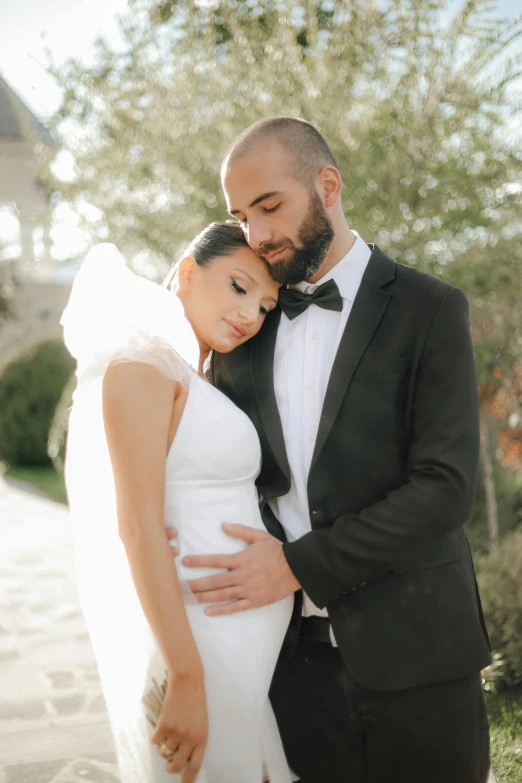 a woman in a white dress and a man in a black suit are hugging