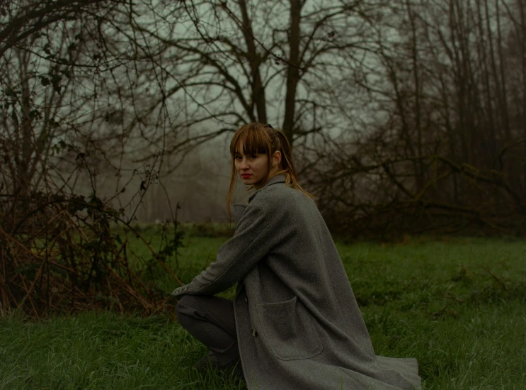 the young woman is sitting in the grass near a tree