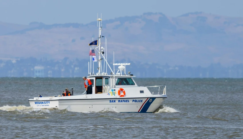 the large boat with flag and some people inside travels down the water