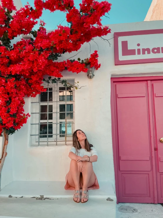 a woman sitting in front of a pink door and pink house