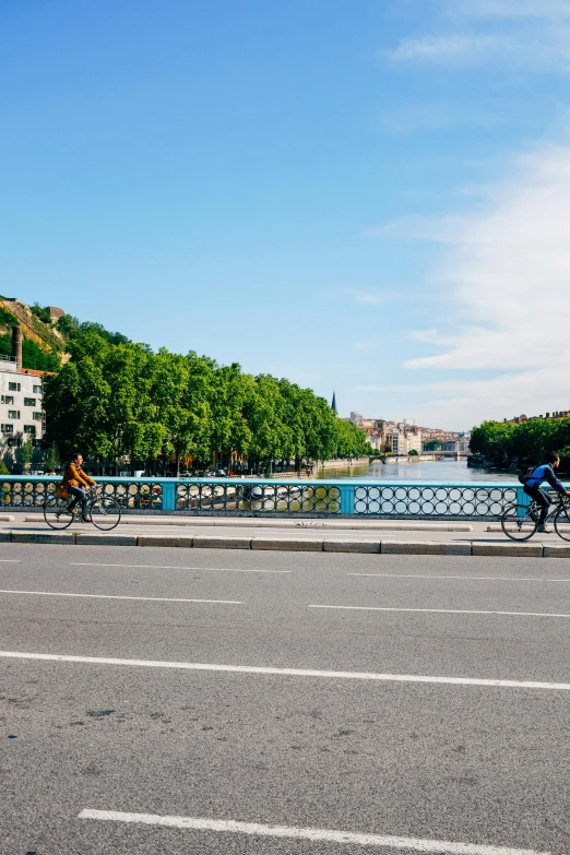 two people riding bicycles down a sidewalk and across the bridge