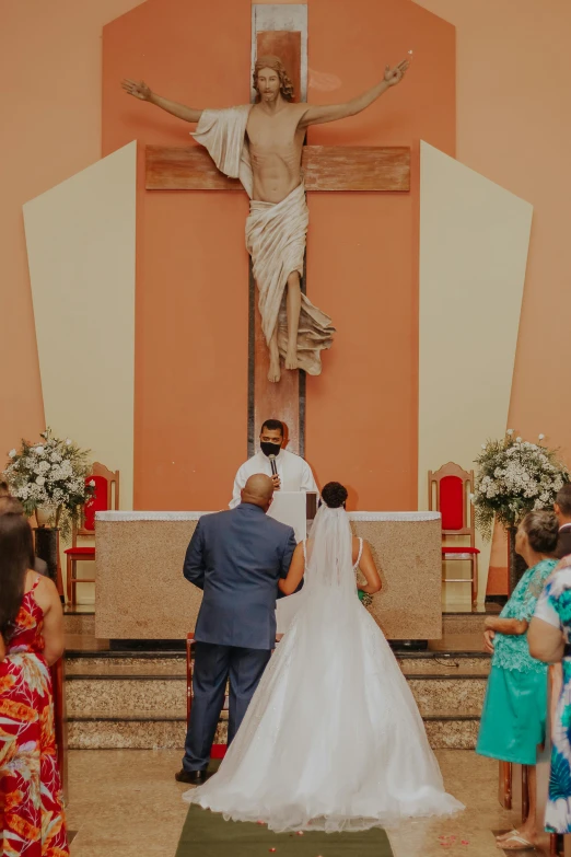 a bride and groom stand in front of a crucifix