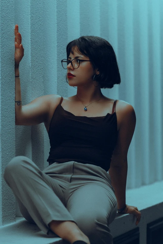 a woman with glasses sitting against a wall