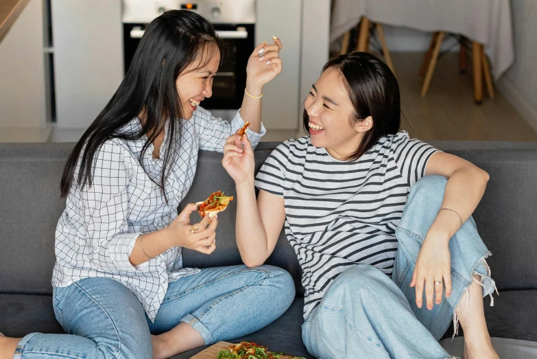 two women sharing pizza on a couch