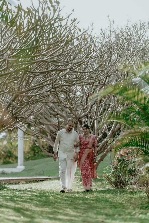 two people walking through the grass between some trees