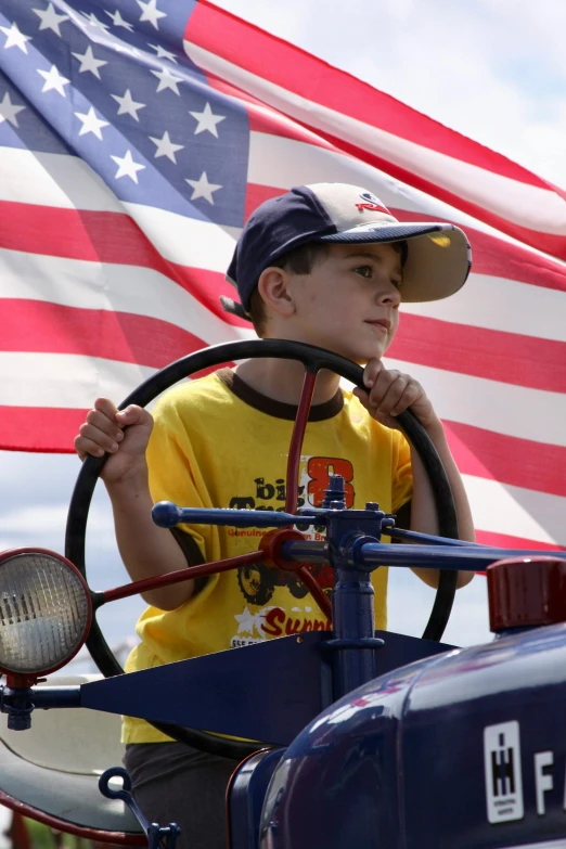 a boy riding on the back of a tractor with an american flag in the background