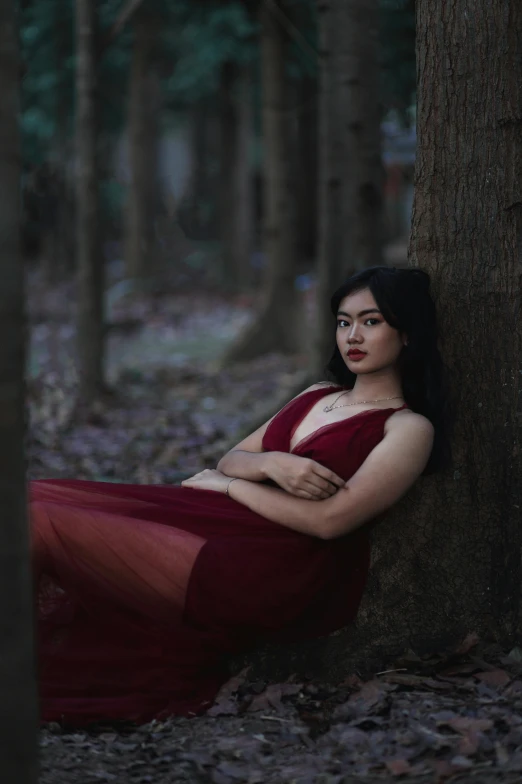 a woman wearing red poses next to a tree