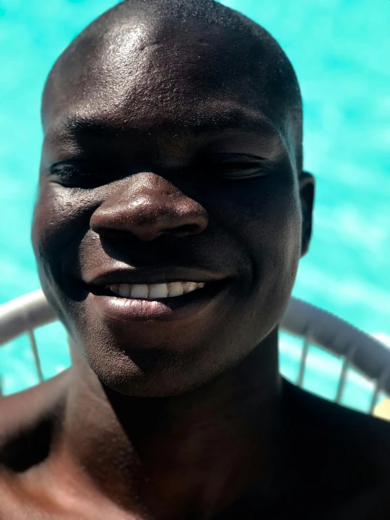 a smiling young man sitting near a swimming pool