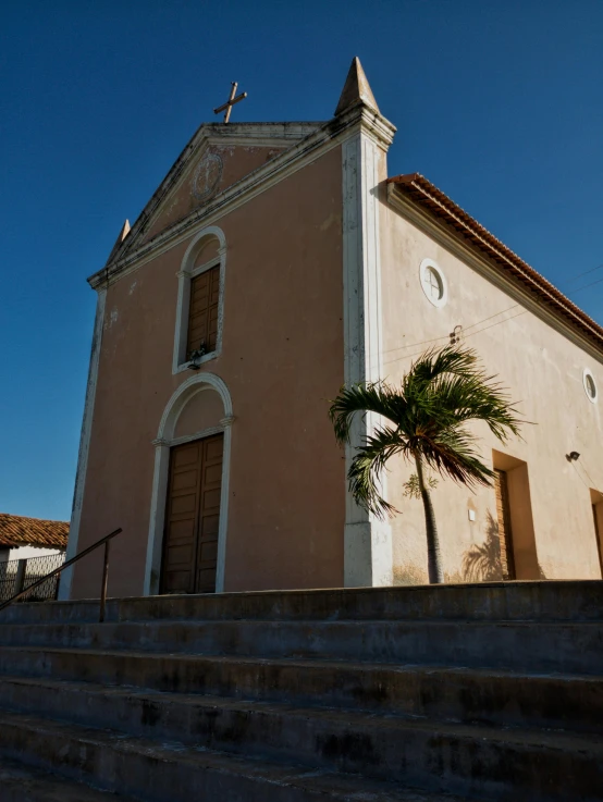 a church with a steeple, stairs and palm tree