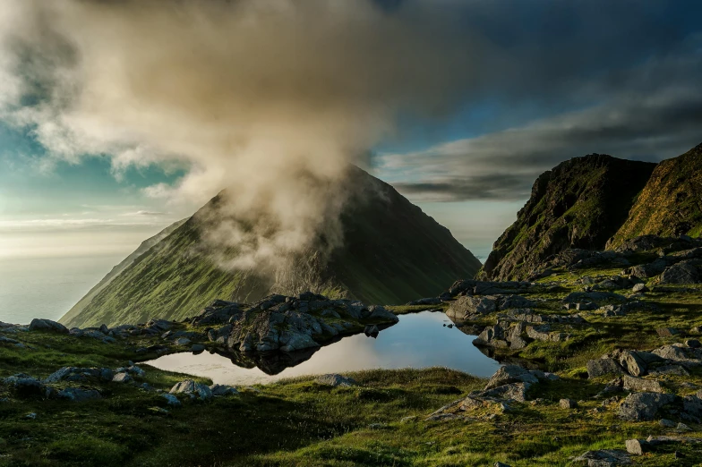 the sun shines on the clouds hovering near a mountain peak