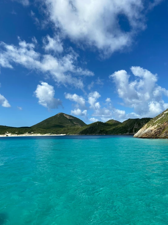 a blue water area with white sand and hills in the background