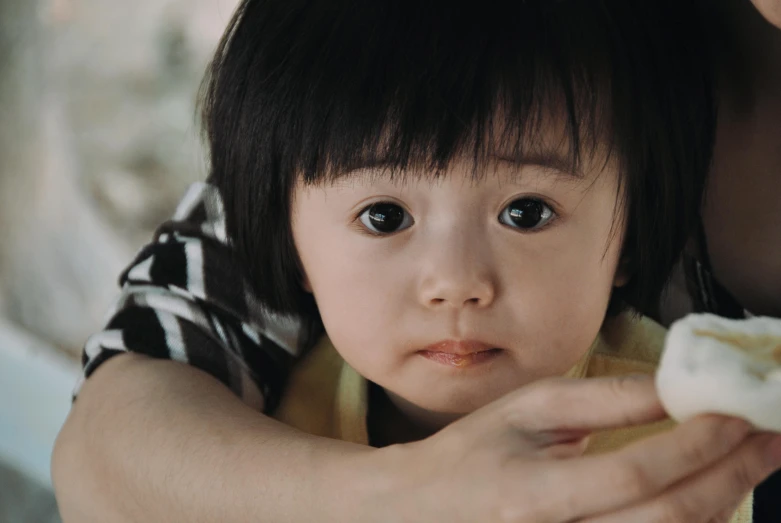 a little girl with black hair holds soing while she has her hands on her shoulder