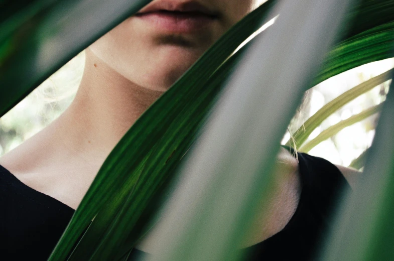 a woman wearing glasses looks out through some green plants