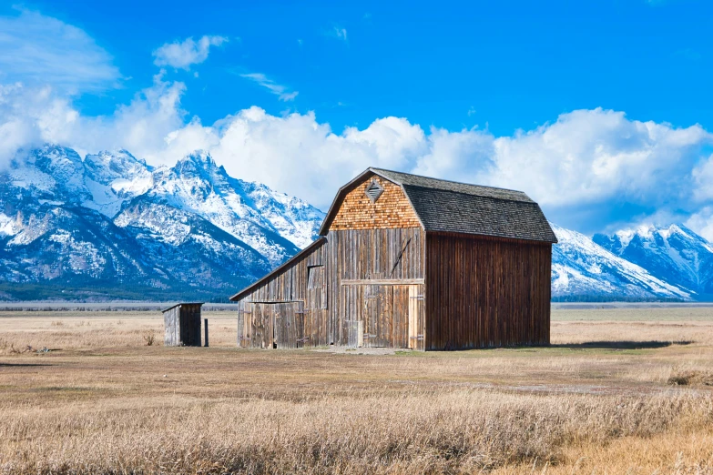 an old barn stands near mountains on a clear day