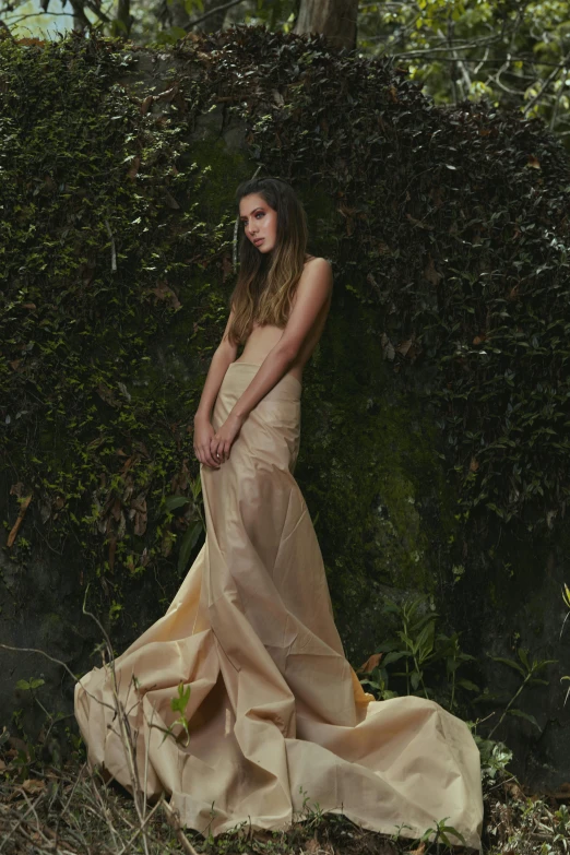 a woman poses in front of bushes, while wearing a long, flowing dress