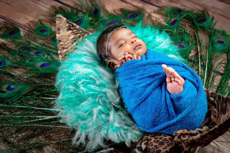 a sleeping baby is wrapped in peacock feathers and wearing a turquoise robe