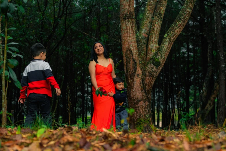 a young woman in a long red dress in the woods with another child