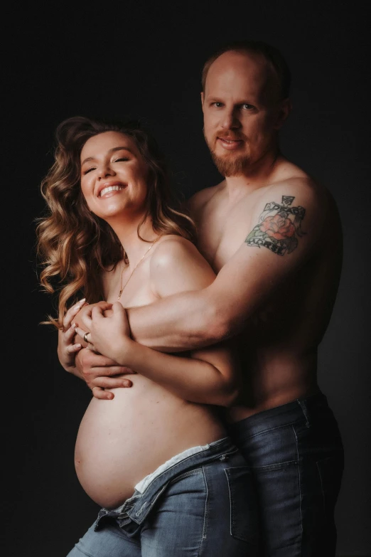 pregnant man in denim pants and tattoos cuddles his pregnant wife's lap