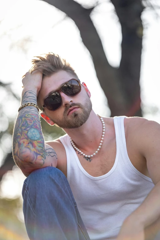 a man wearing sunglasses with tattoos is sitting on a stone