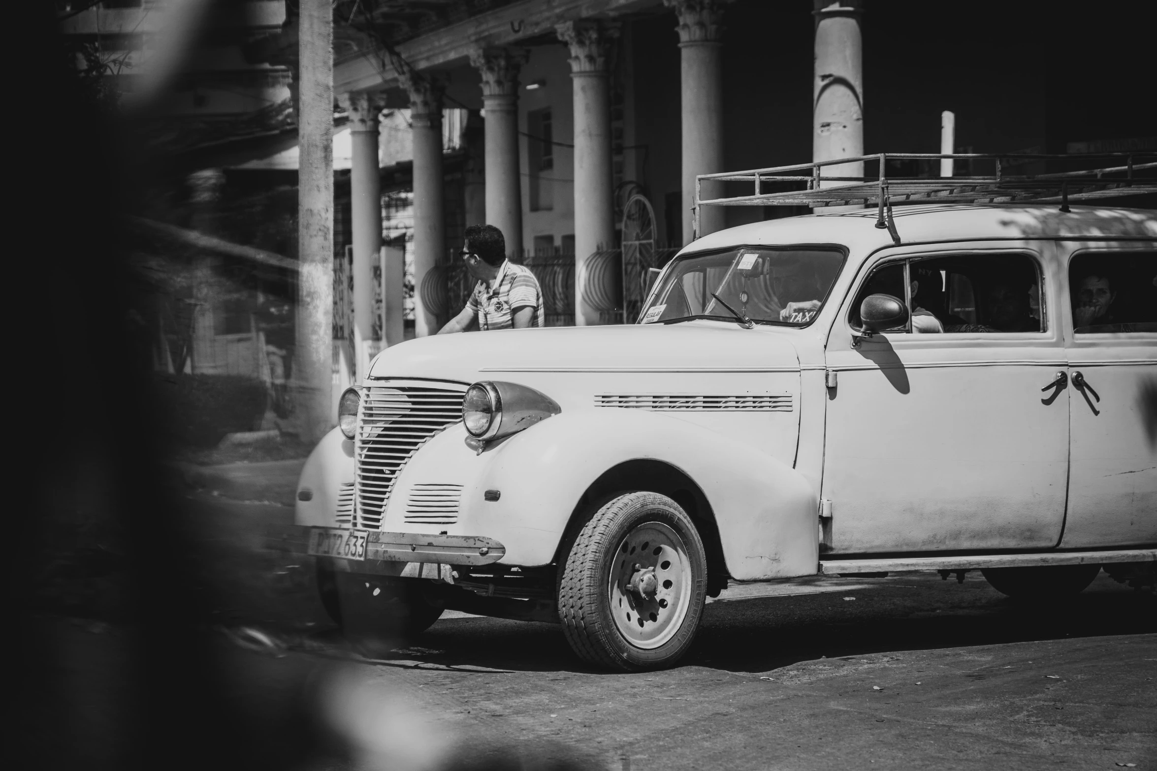 a black and white po shows an old car in a row with people standing around