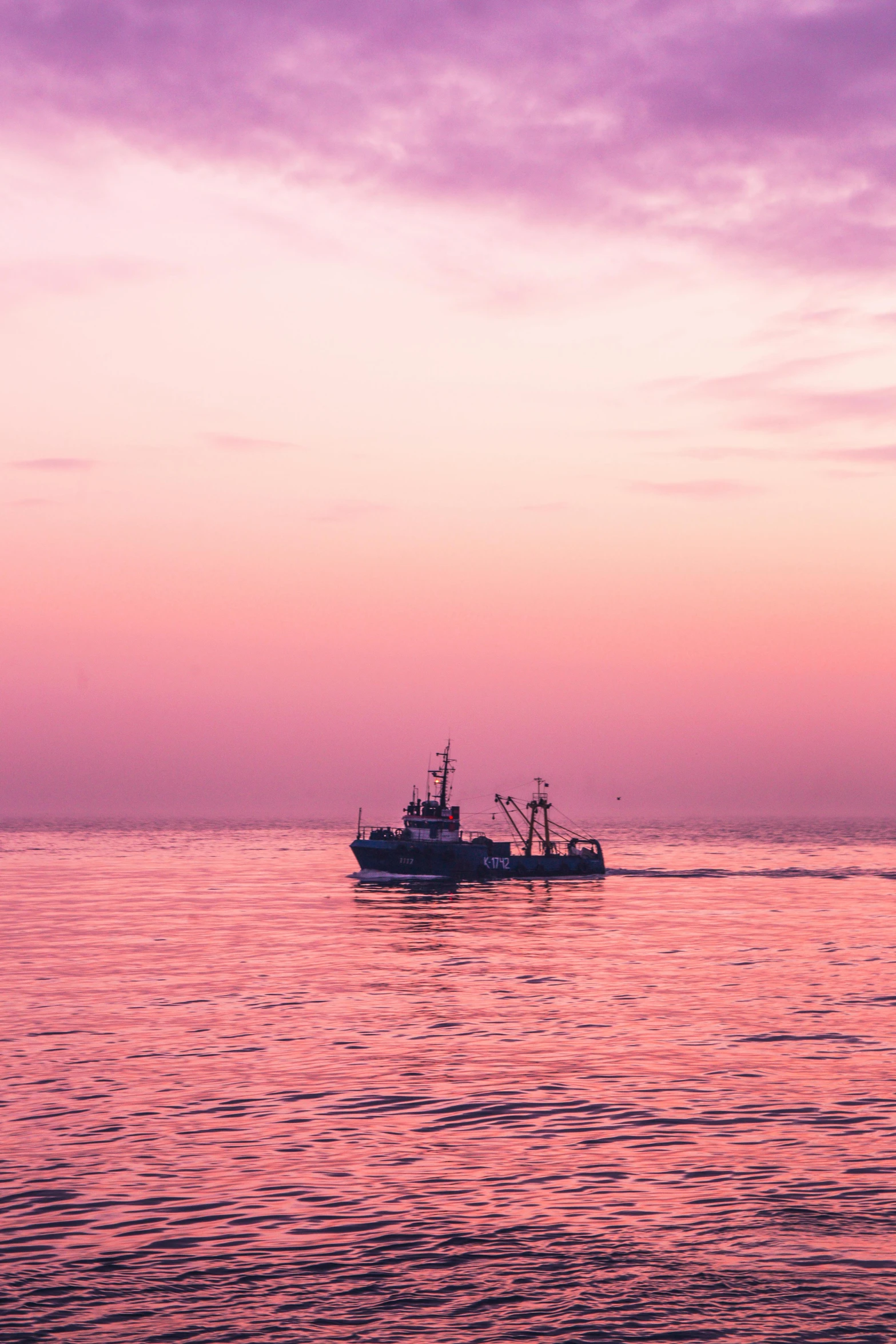 a boat is floating across the ocean with pink and purple clouds