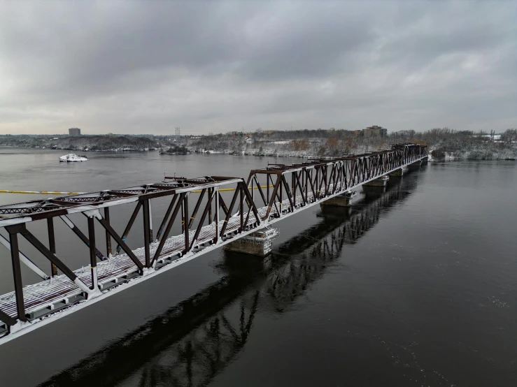 the train bridge crosses a river with a snow covered hill in the background