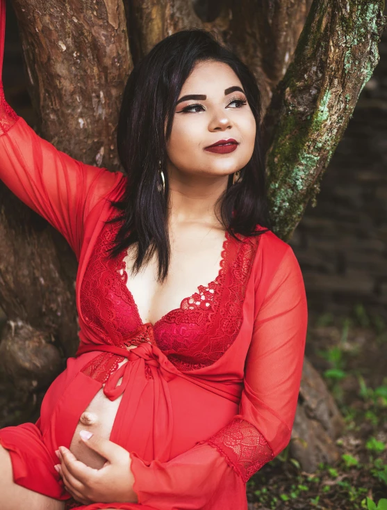 a woman in a red gown is sitting near the tree