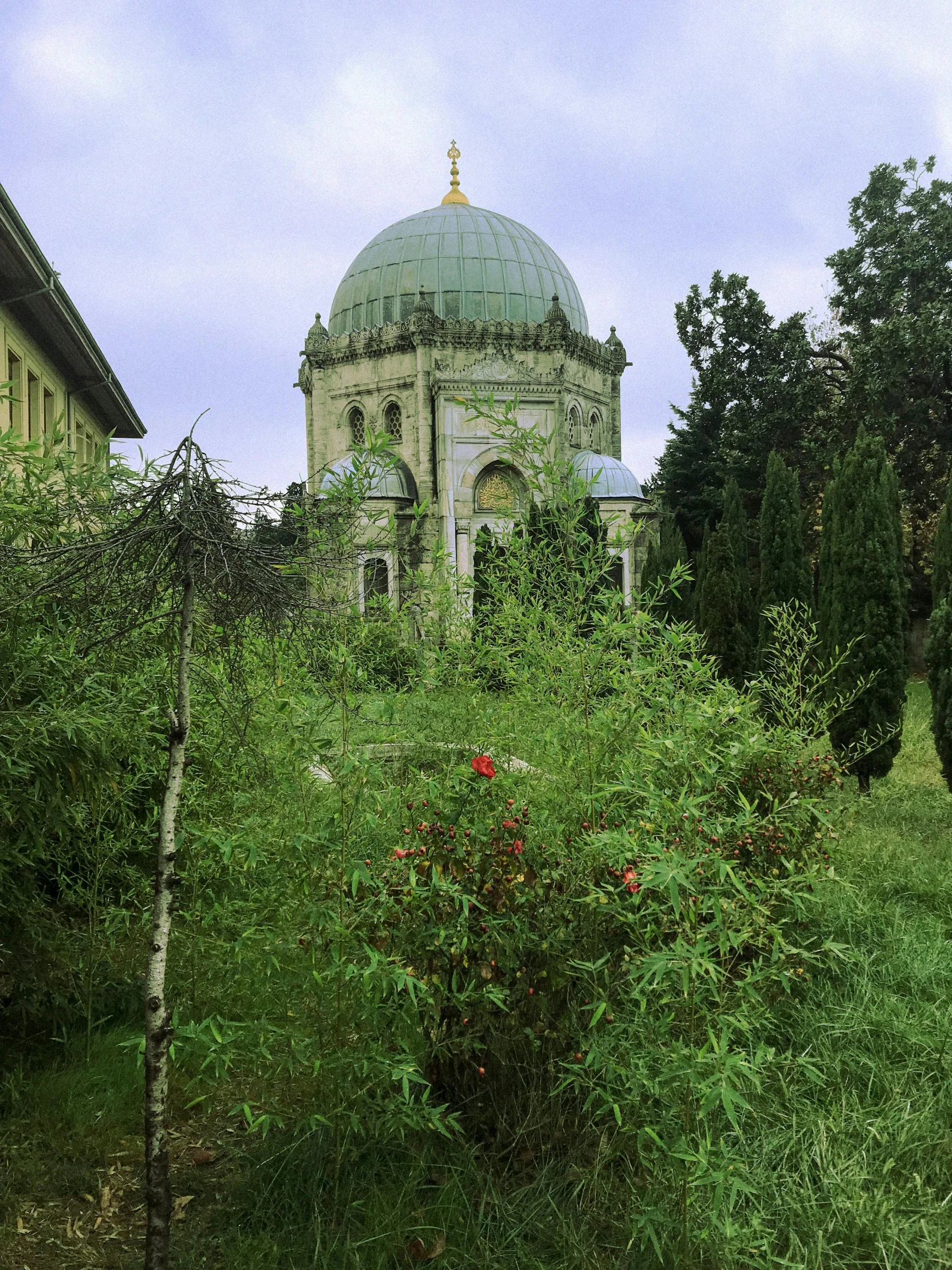 an old, run down church among some trees and flowers