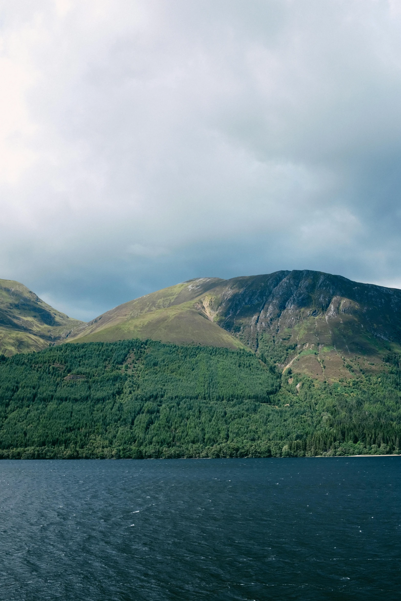 mountain with lake below during cloudy day on cloudy day