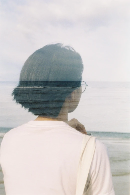 the back view of a woman standing on the beach looking out to sea