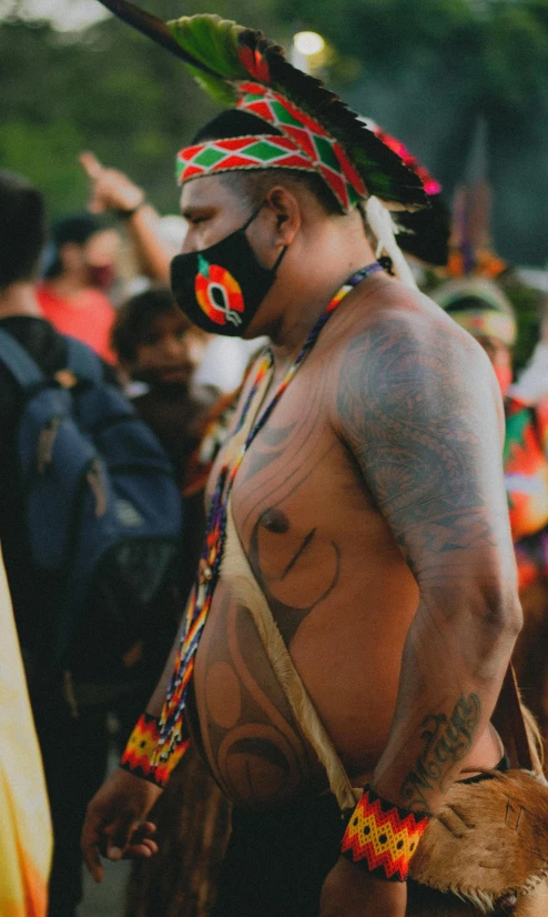 a tattooed man wearing a headdress and a face mask