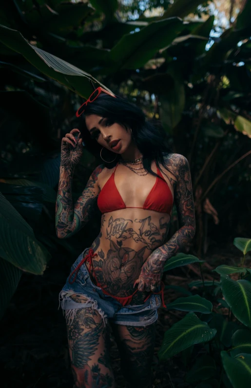 tattooed woman standing next to some vegetation in the sun