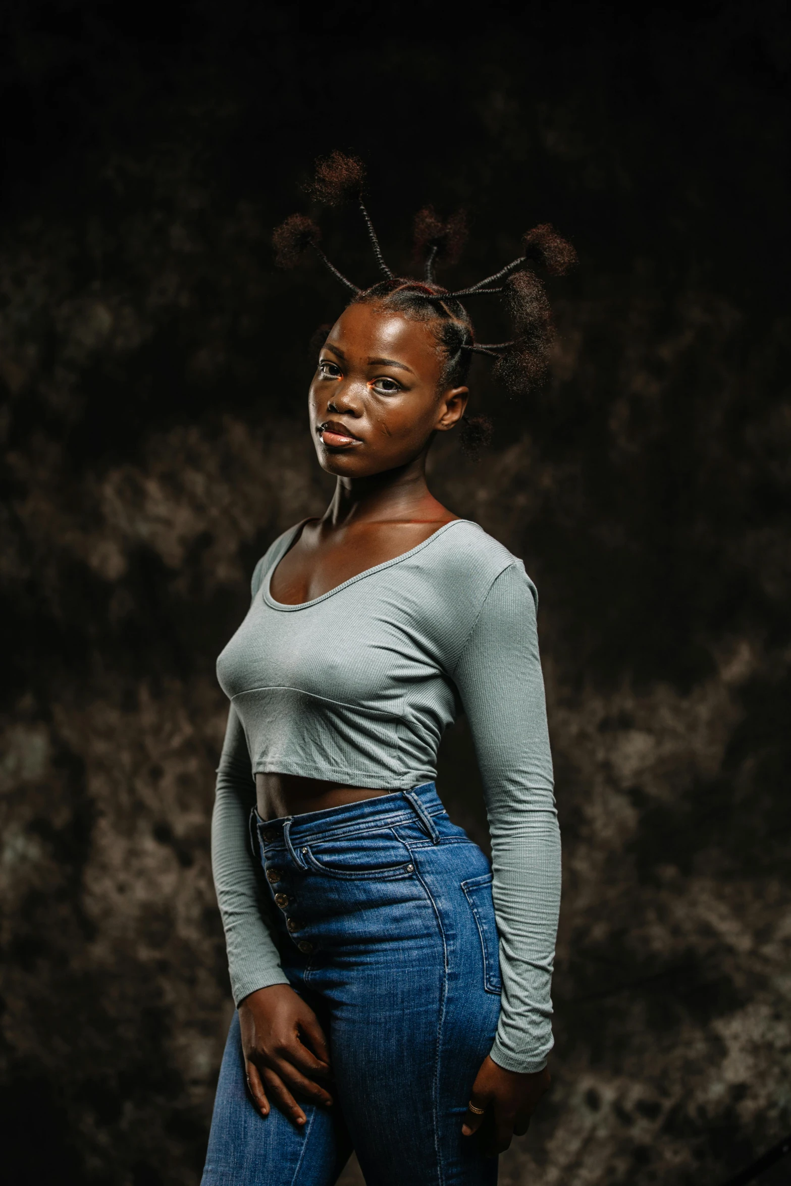 a woman with an unusual hair style poses in a grey shirt