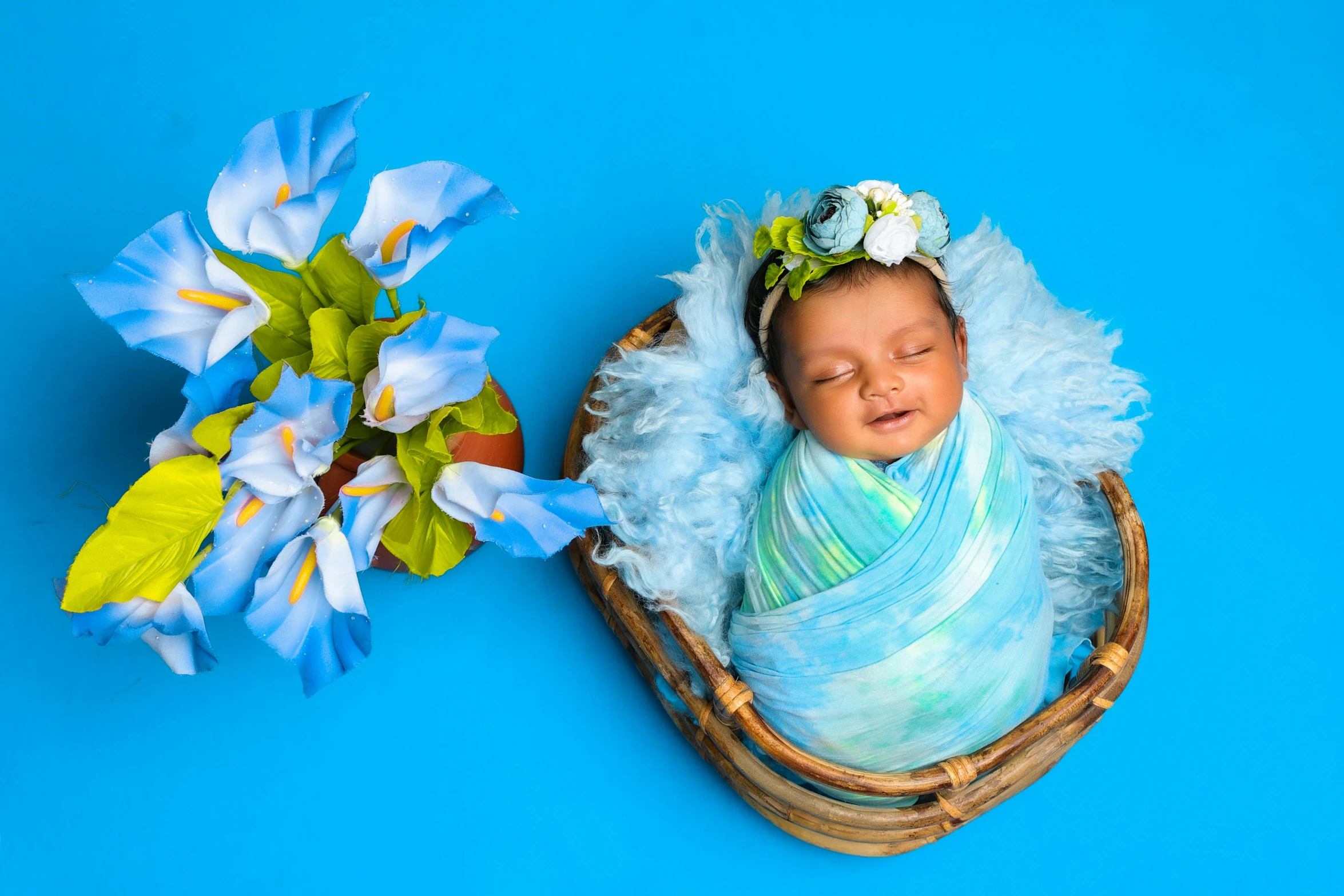 a newborn in a blue wrap and a vase with flowers