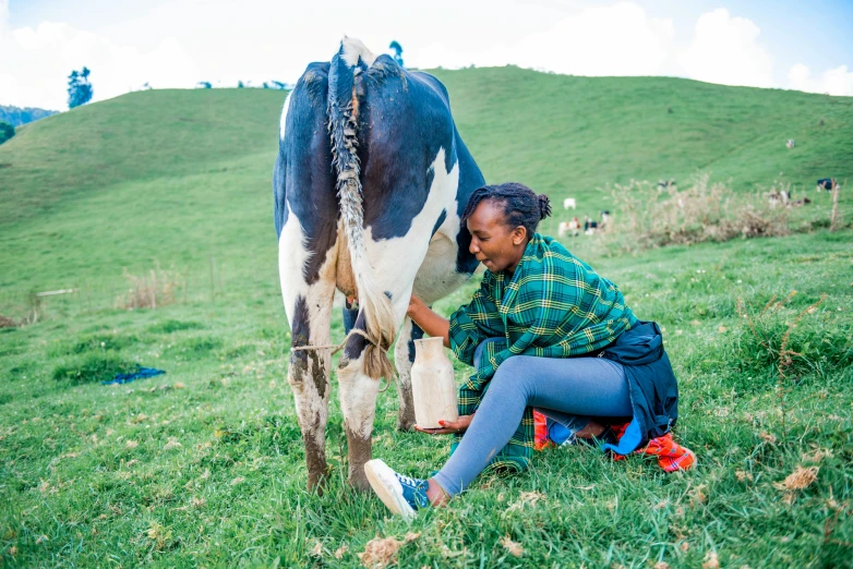 a woman kneels down as she pets a black and white cow