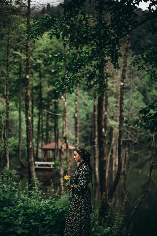 a woman stands in the forest and holds a small flower