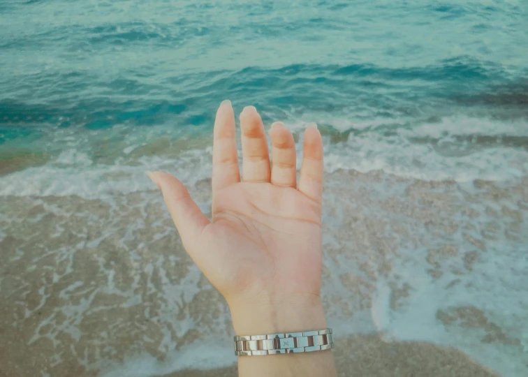 a person is holding up their hand on the beach