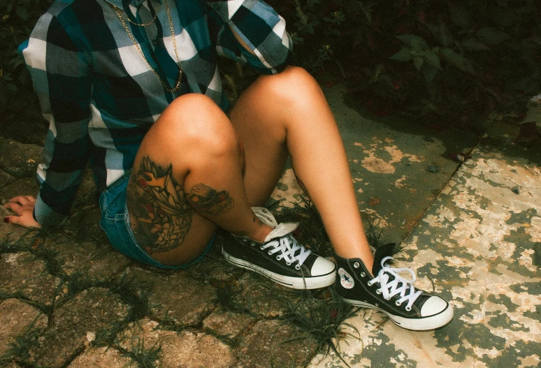 a man with tattoos sitting on a stone area wearing black and white shoes