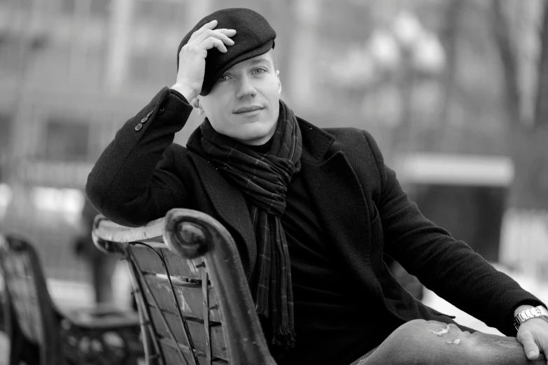 black and white image of man wearing coat sitting on bench