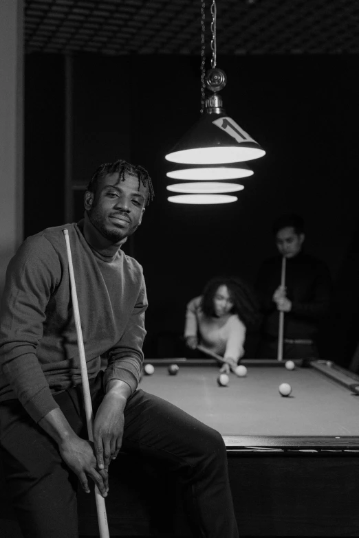 a man is sitting in a dark room near a pool table