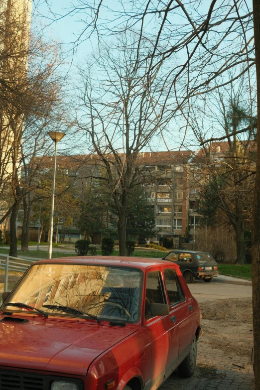 a red car is parked next to trees