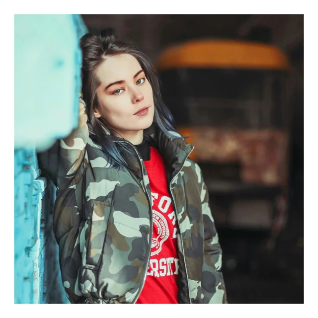 a woman in camouflage print jacket leaning against a blue wall