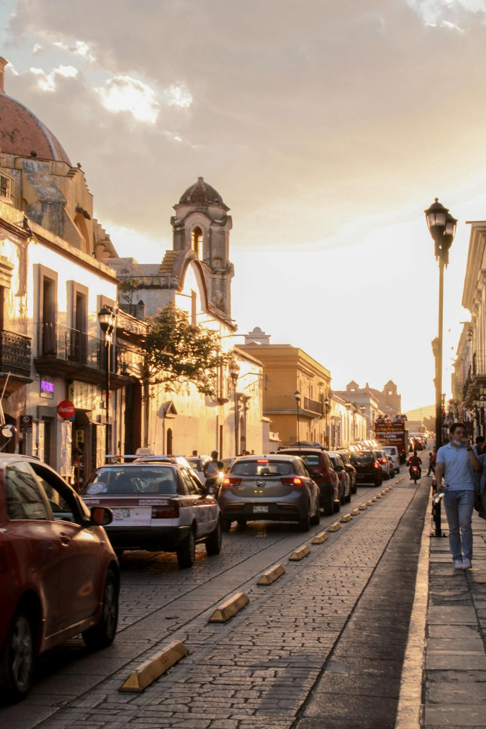 an old street with cars and people walking along the sidewalk