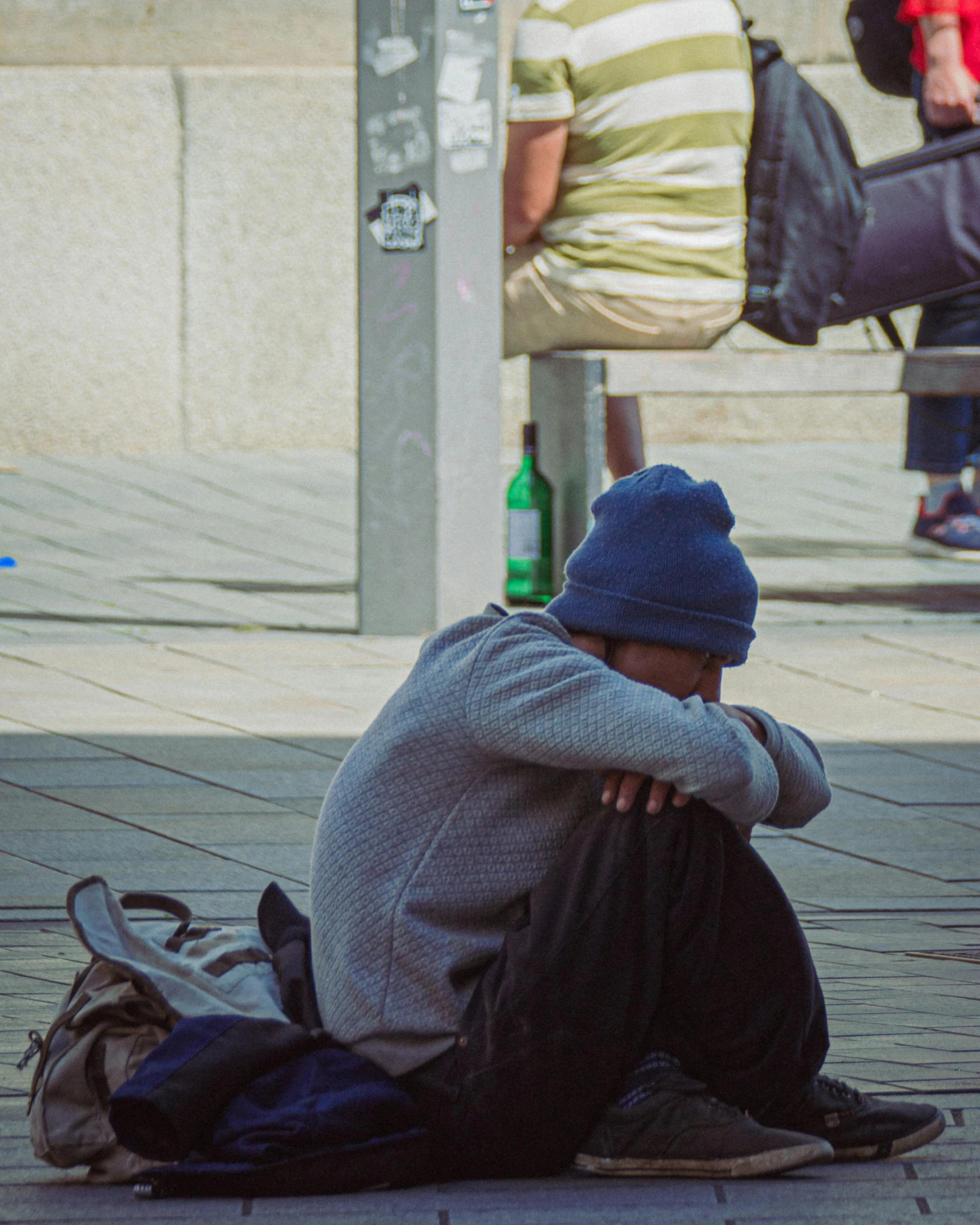 a man sitting on the sidewalk near a bench