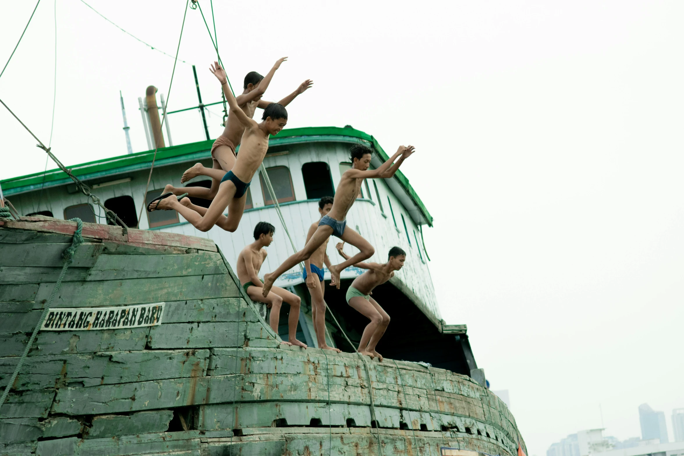 young men are jumping off the bow of an old boat