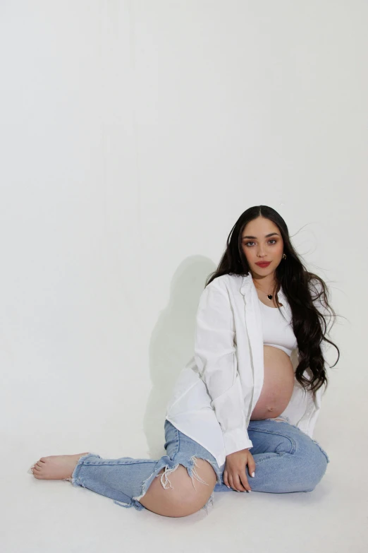 a pregnant woman with a white jacket and jeans is posing for a portrait