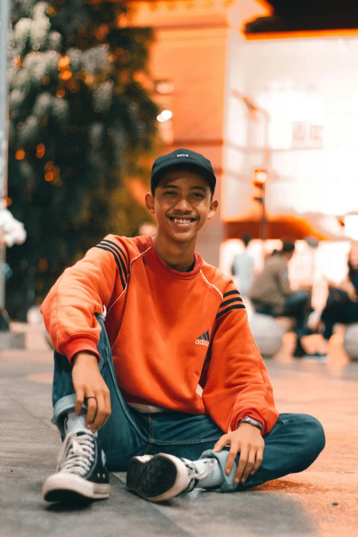 a young man sitting on the floor in a city square smiling