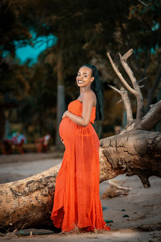 a pregnant woman in an orange dress standing on top of a tree