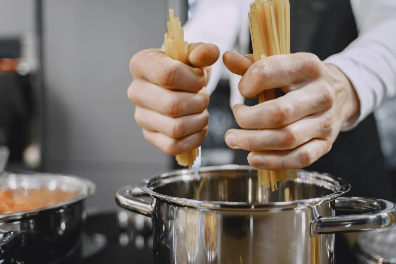 two people hold up a pair of wooden tongs to stir pasta