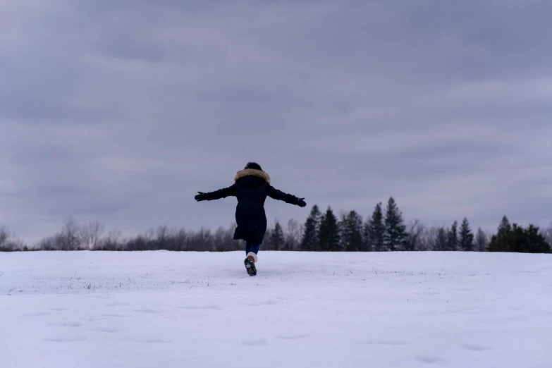 person in long coat playing in snow with trees behind